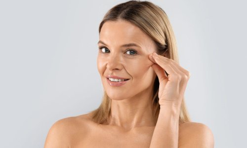 Plastic surgery, face-lift, blepharoplasty, aesthetic medicine. Closeup shot of attractive blonde half-naked middle aged woman playing with her face skin, isolated on studio background, copy space